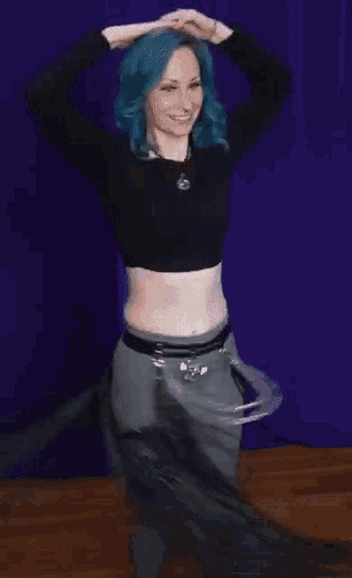 a woman with blue hair wearing a black crop top and grey pants