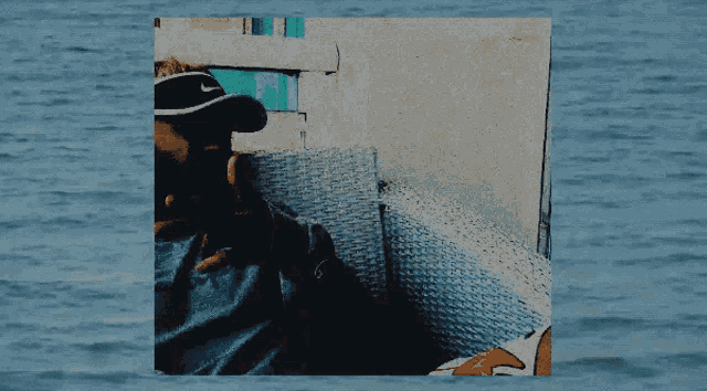 a man wearing a nike hat sits in a chair in front of a body of water