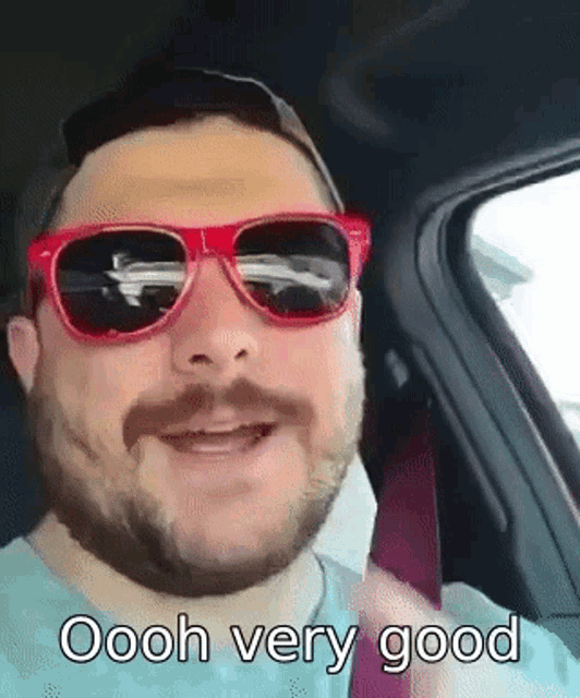 a man wearing red sunglasses and a hat is sitting in a car and says oooh very good .