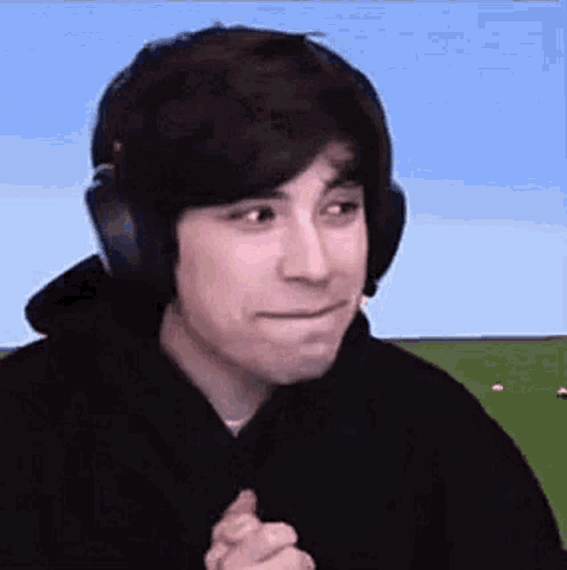 a man wearing headphones and a black hoodie is making a face .