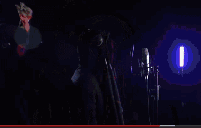 a man is singing into a microphone with a purple light behind him