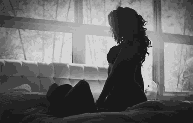 a silhouette of a woman sitting on a bed in front of a window