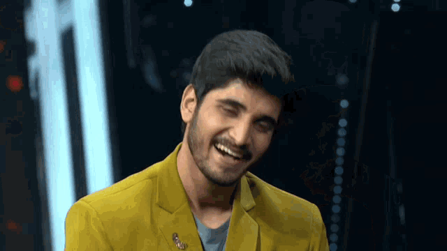 a man wearing a yellow jacket and a blue shirt smiles