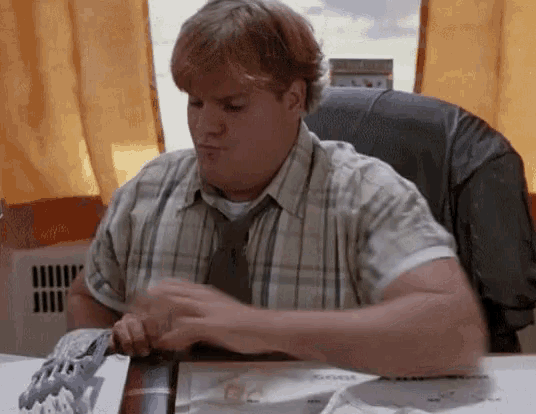 a man in a plaid shirt and tie sitting at a desk