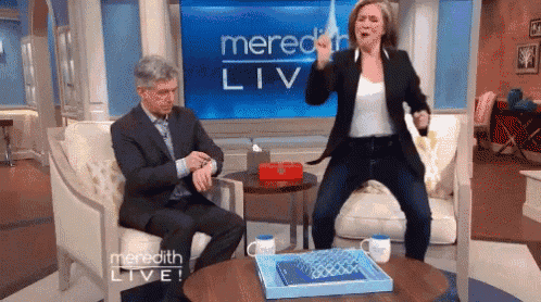 a man sits in a chair while a woman stands in front of a screen that says meredith live