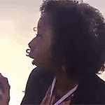 a woman with curly hair is wearing a lanyard around her neck and holding a pen .