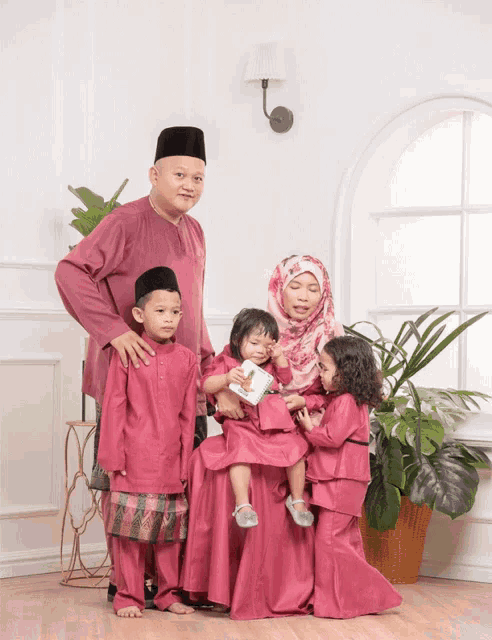 a family is posing for a picture in front of a window and a plant