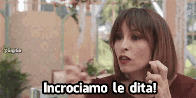 a woman is sitting at a table with the words incrociamo le dita written on her face .