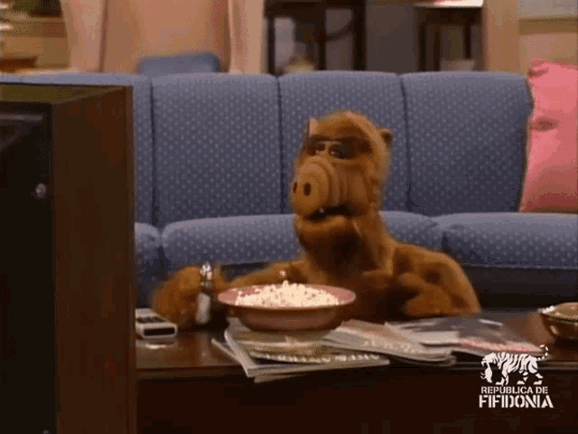 a stuffed animal sitting on a couch eating popcorn from a bowl