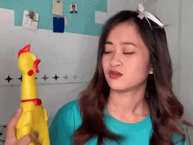 a woman in a blue shirt is holding a rubber chicken .