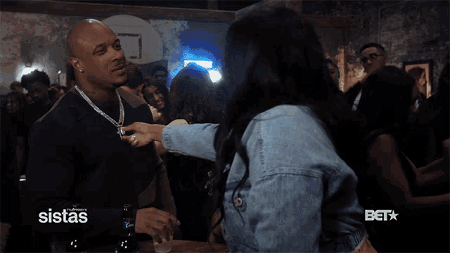 a man talking to a woman in a crowd with sistas on the bottom right