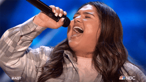 a woman singing into a microphone with the nbc logo in the corner