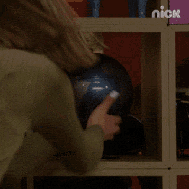 a young boy looks out from behind a shelf with a nick logo on it