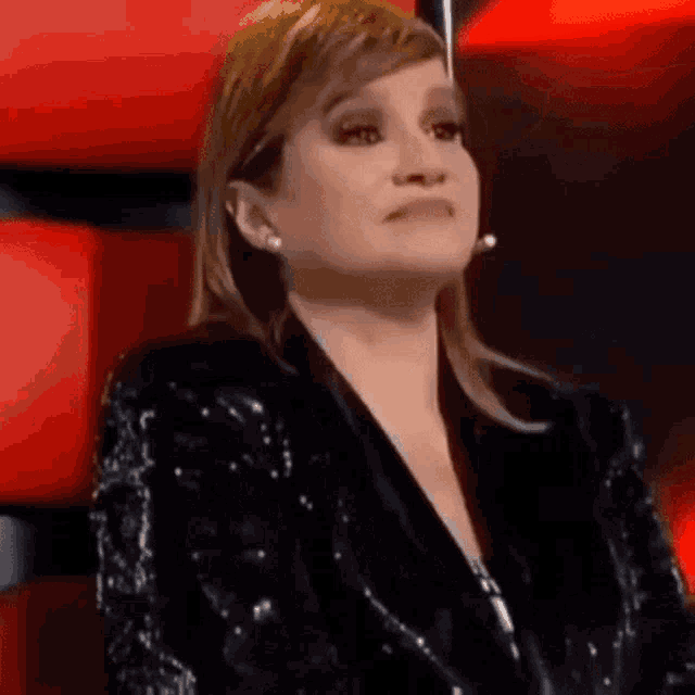 a woman in a black sequined jacket is sitting in a red chair with her eyes closed .