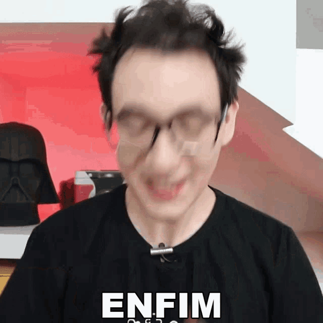 a man wearing glasses and a black shirt has the word enfim on his shirt