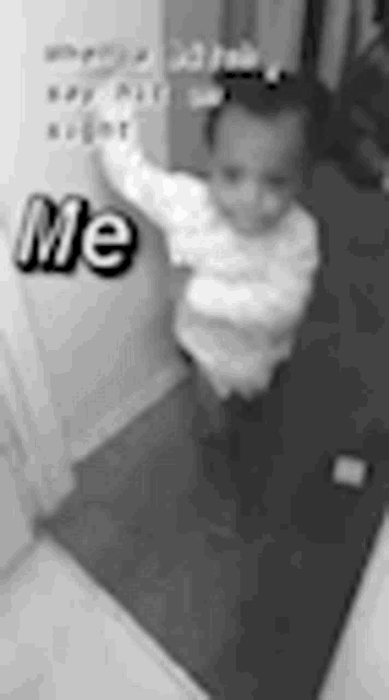 a black and white photo of a baby standing next to a door with the words `` me '' on it .