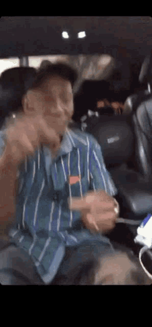 a man in a striped shirt is sitting in the back seat of a car holding a cigarette .
