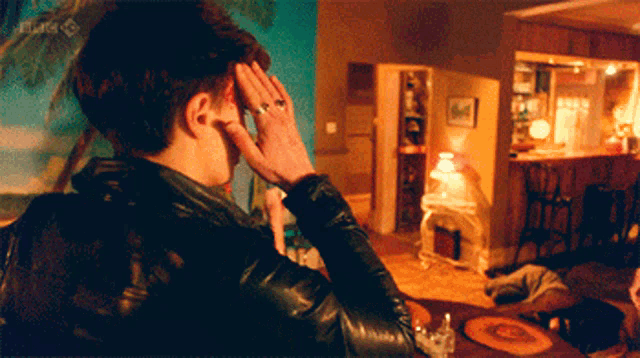 a man in a leather jacket holds his head in a living room