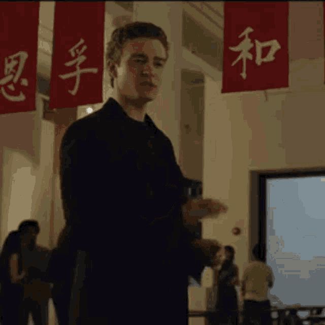 a man in a black suit is standing in front of a red banner with chinese characters on it