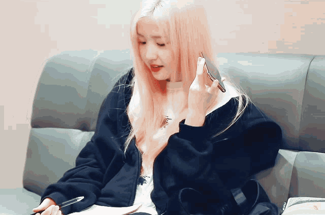 a girl with pink hair is sitting on a couch holding a cell phone