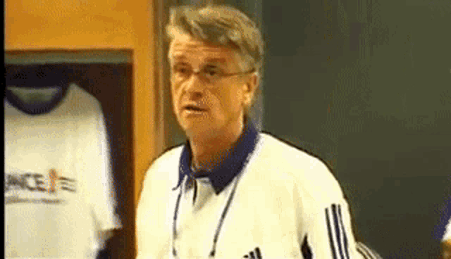 a man in a white adidas jacket stands in front of a wall with shirts hanging on it