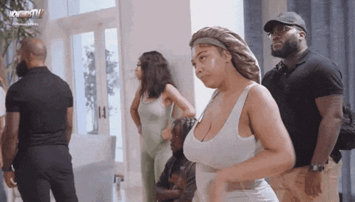 a woman in a white tank top is standing in a room with a group of people .