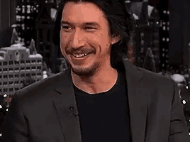 a man wearing a suit and a black shirt is smiling .