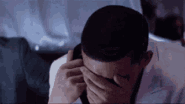 a man is covering his eyes with his hand while talking on a cell phone .