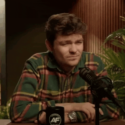 a man in a plaid shirt is sitting at a table with a microphone in front of him .