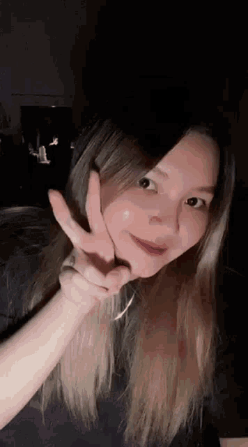 a young woman is making a peace sign with her hand in front of her face .