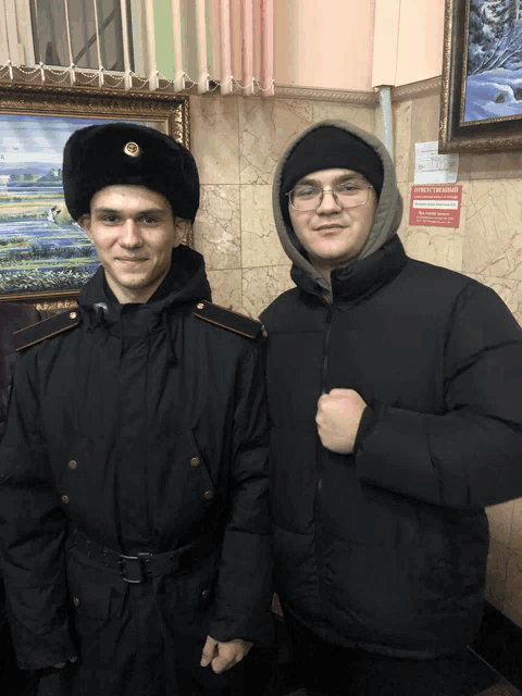 a man in a hooded jacket stands next to a man in a black uniform