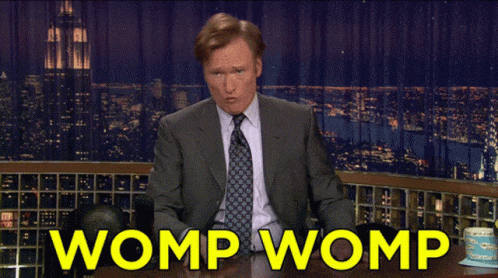 a man in a suit and tie is sitting at a table with the words womp womp behind him