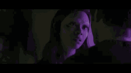a man and a woman are kissing in a dark room in a purple light .