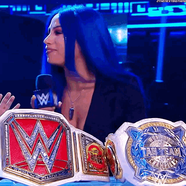 a woman with blue hair is holding two wrestling belts