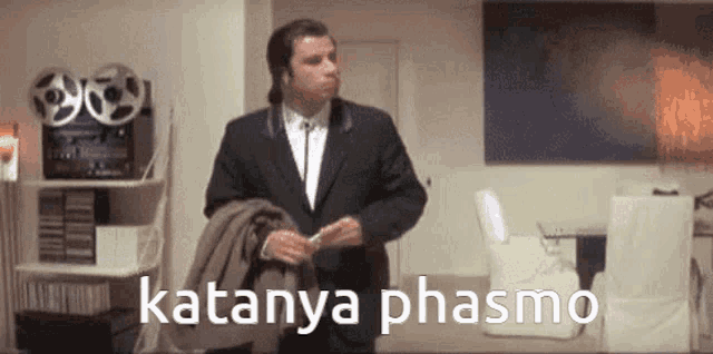 a man in a suit and tie is standing in a room with the words katanya phasmo written on the bottom