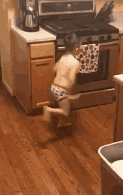 a baby in a diaper is standing in front of an oven in a kitchen