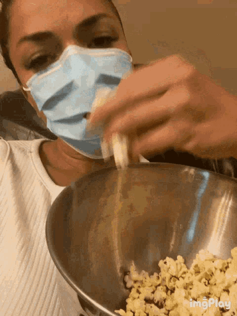 a woman wearing a face mask is pouring popcorn into a metal bowl