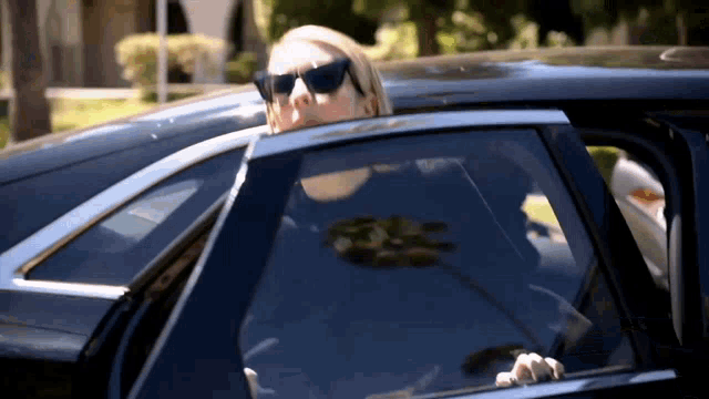 a woman wearing sunglasses is peeking out of a car window