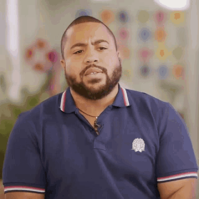 a man with a beard is wearing a blue polo shirt with a logo on the front