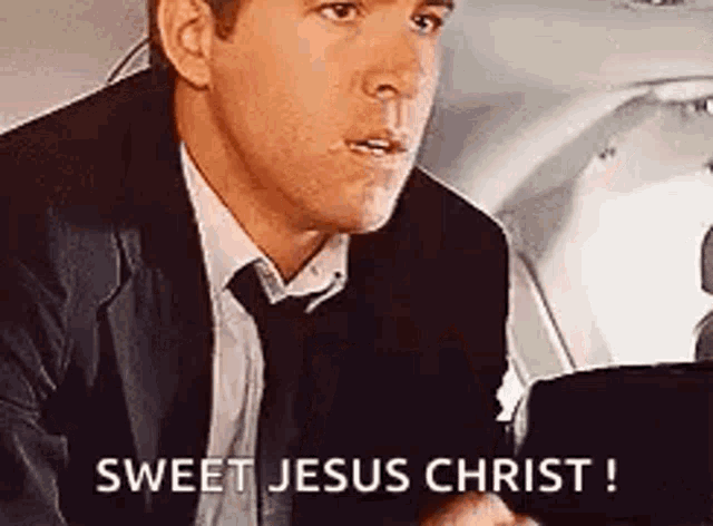 a man in a suit and tie is sitting on a plane and says `` sweet jesus christ '' .