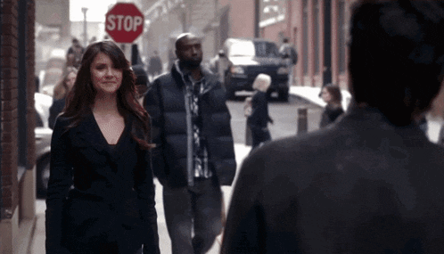 a woman walking down a street with a stop sign behind her