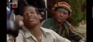 a man wearing a rasta hat is sitting next to another man in a car .