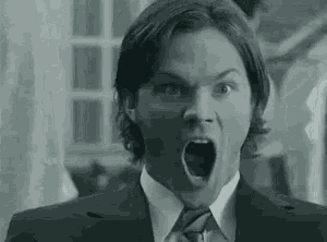 a man in a suit and tie is making a funny face with his mouth open .