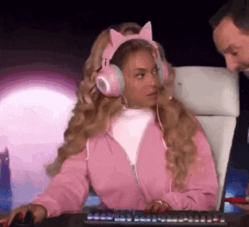 a woman wearing pink headphones and a pink jacket is sitting at a computer keyboard .