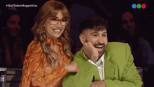 a man in a green suit is laughing next to a woman in an orange dress with glasses