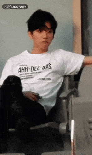 a man in a white t-shirt is sitting in a chair .