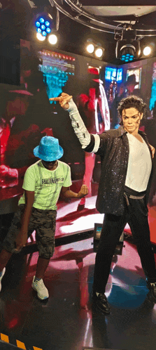 a boy wearing a green shirt that says streetwear stands in front of a wax figure of michael jackson