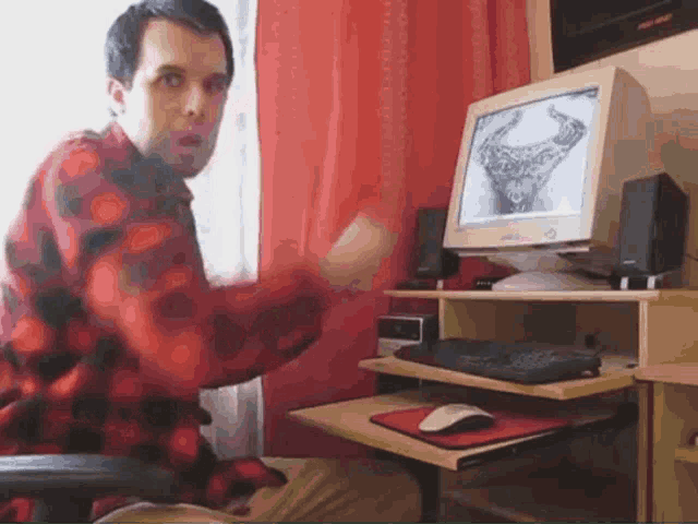 a man in a red plaid shirt sitting in front of a computer monitor