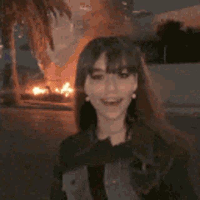 a young woman is smiling in front of a palm tree and a fire .