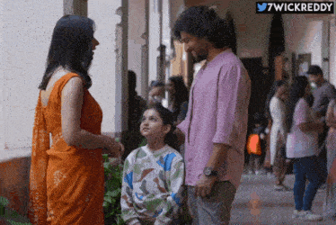 a man in a pink shirt stands next to a woman in an orange dress and a little girl
